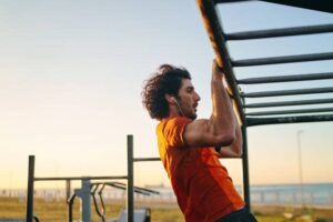 Sporty young man doing pull-ups in morning at the outdoors gym at his local park