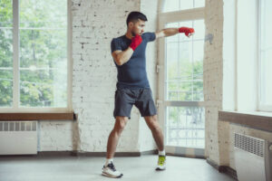 Kick, punch up. Young caucasian man training at home during quarantine of coronavirus outbreak, doing exercises of fitness, box. Staying sportive during insulation. Wellness, sport, movement concept.