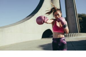 Sportswoman doing boxing working outdoors. Female practicing boxing, throwing a punch in front.